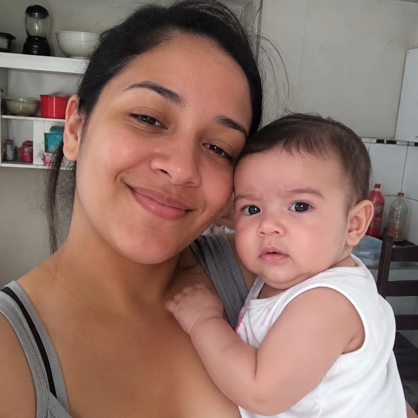 Carla com seu bebê no colo na cozinha de casa